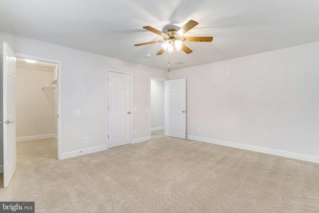 unfurnished bedroom featuring a ceiling fan, baseboards, a spacious closet, a closet, and light colored carpet