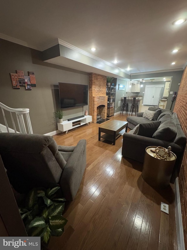 living room with a fireplace, ornamental molding, brick wall, and hardwood / wood-style flooring