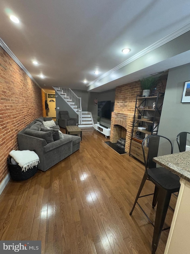 living room with crown molding, wood-type flooring, brick wall, and a brick fireplace