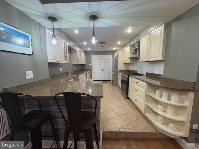 kitchen featuring wall chimney exhaust hood, kitchen peninsula, decorative backsplash, white cabinets, and appliances with stainless steel finishes