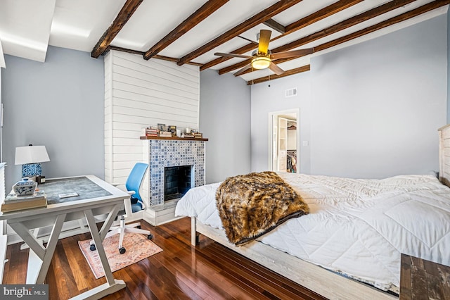 bedroom featuring beamed ceiling, ceiling fan, dark hardwood / wood-style flooring, and a tile fireplace