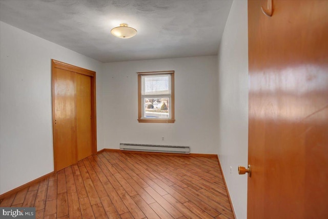 empty room with light wood-type flooring and a baseboard heating unit