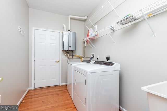 clothes washing area featuring water heater, sink, light hardwood / wood-style floors, and washer and dryer