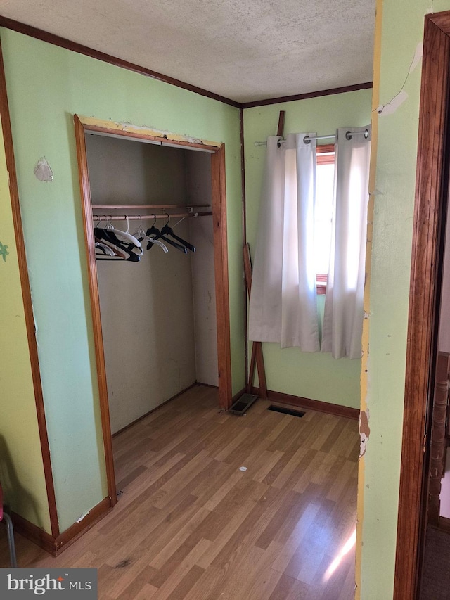 unfurnished bedroom featuring crown molding, a closet, a textured ceiling, and light wood-type flooring