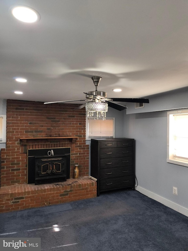 unfurnished living room with a brick fireplace, ceiling fan, and dark colored carpet