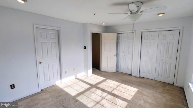 unfurnished bedroom with light carpet, two closets, and ceiling fan