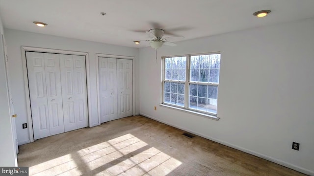 unfurnished bedroom with multiple closets, ceiling fan, and light colored carpet