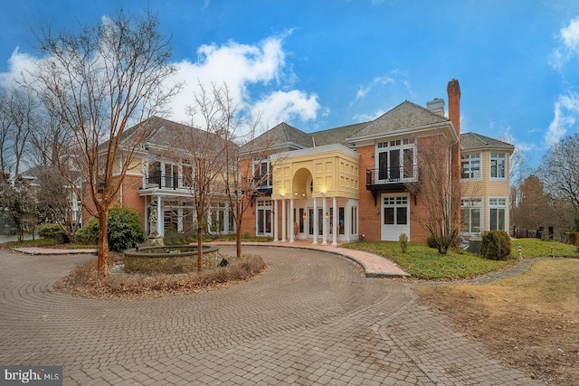 view of front of house with brick siding, curved driveway, and a chimney