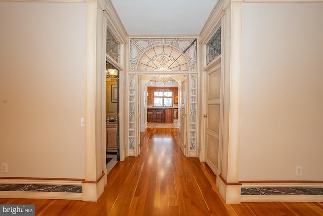 hall featuring arched walkways, a notable chandelier, baseboards, and wood finished floors