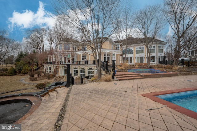 back of property featuring a patio, a chimney, a hot tub, a balcony, and an outdoor pool