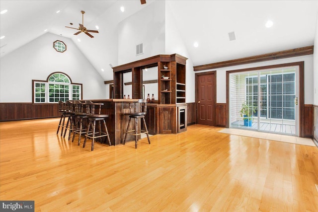 bar with a towering ceiling, light hardwood / wood-style flooring, and ceiling fan