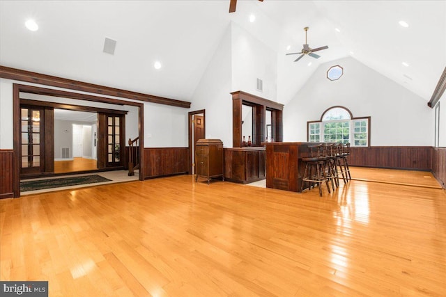 interior space featuring wood walls, french doors, ceiling fan, light wood-type flooring, and a towering ceiling