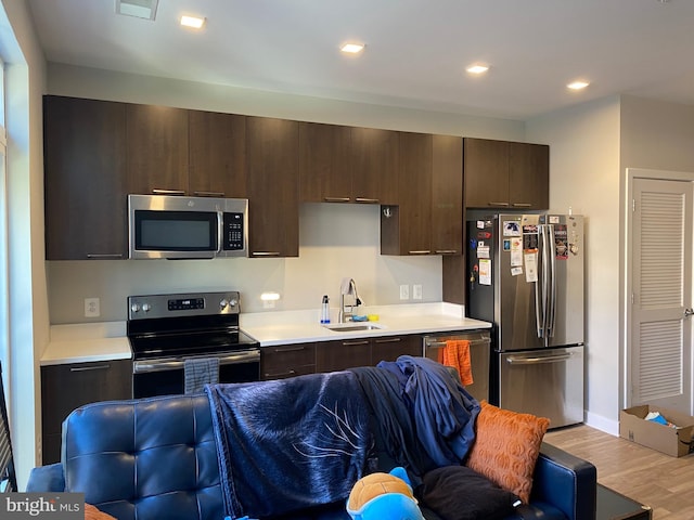 kitchen with appliances with stainless steel finishes, sink, dark brown cabinets, and light wood-type flooring