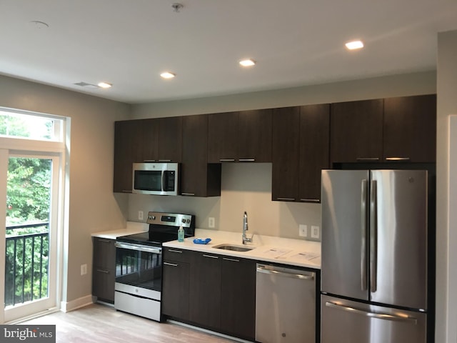 kitchen featuring dark brown cabinetry, appliances with stainless steel finishes, sink, and light hardwood / wood-style flooring