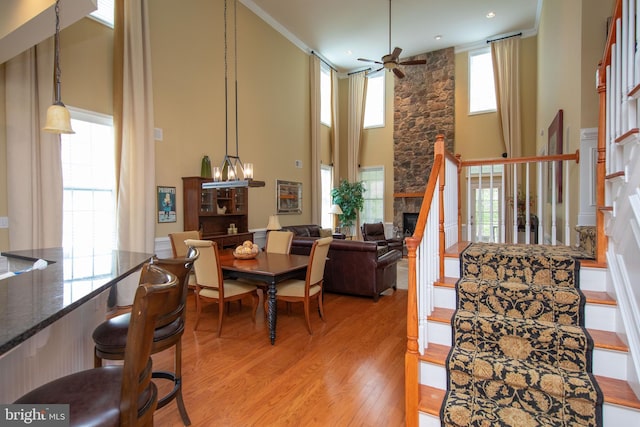 dining area with plenty of natural light, a stone fireplace, ceiling fan with notable chandelier, and light hardwood / wood-style flooring