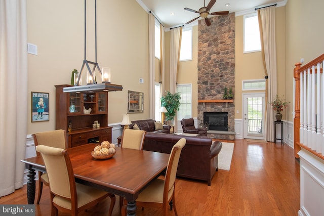 dining space with ceiling fan with notable chandelier, light wood-type flooring, a towering ceiling, and a stone fireplace