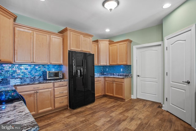 kitchen with light brown cabinets, tasteful backsplash, black fridge, dark hardwood / wood-style floors, and dark stone counters