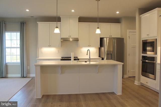 kitchen featuring an island with sink, appliances with stainless steel finishes, and decorative light fixtures