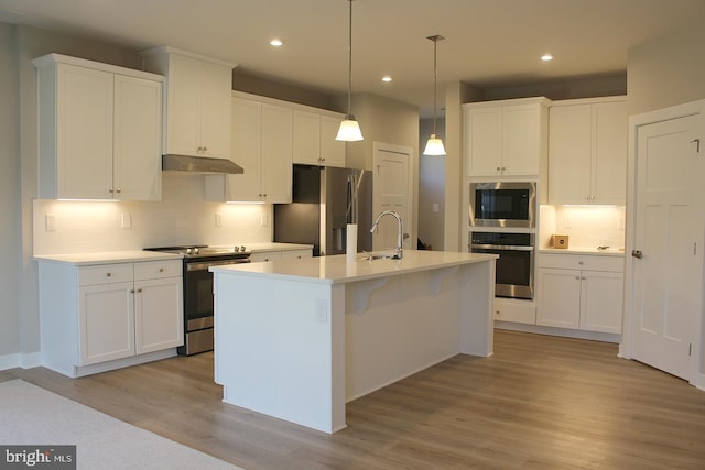 kitchen with appliances with stainless steel finishes, a kitchen island with sink, hanging light fixtures, light hardwood / wood-style floors, and white cabinets