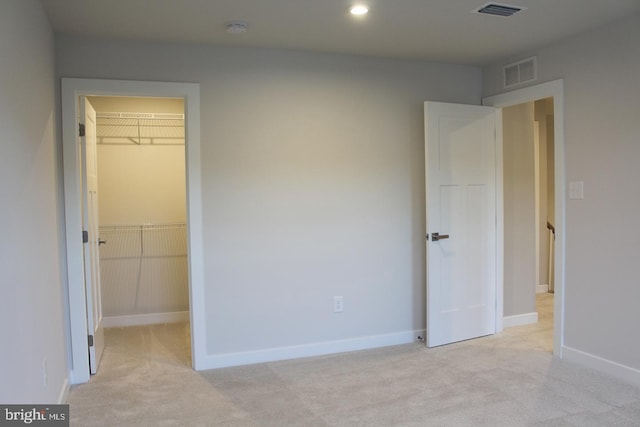 unfurnished bedroom featuring a spacious closet, light colored carpet, and a closet