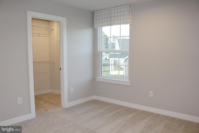 unfurnished bedroom featuring a spacious closet, light colored carpet, and a closet