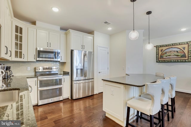 kitchen featuring tasteful backsplash, dark stone counters, stainless steel appliances, decorative light fixtures, and white cabinetry