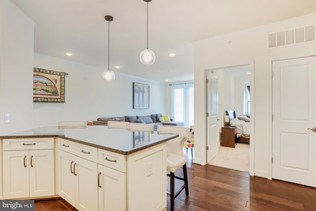 kitchen featuring hanging light fixtures, dark hardwood / wood-style flooring, kitchen peninsula, dark stone countertops, and a kitchen bar