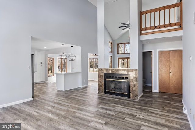 unfurnished living room featuring ceiling fan with notable chandelier, high vaulted ceiling, a fireplace, and hardwood / wood-style flooring