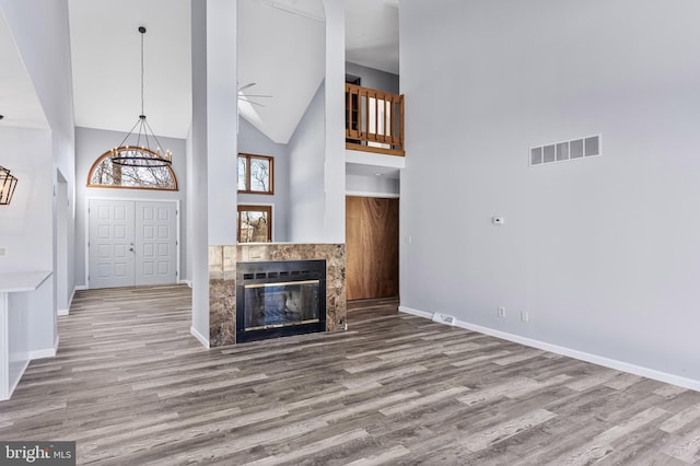 unfurnished living room featuring a high ceiling, a fireplace, ceiling fan, and wood-type flooring