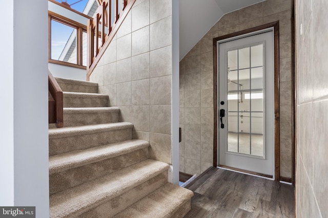 staircase with tile walls, hardwood / wood-style floors, and vaulted ceiling