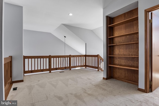 bonus room with lofted ceiling, light carpet, and built in shelves