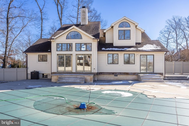 rear view of property featuring a covered pool, central air condition unit, and a patio