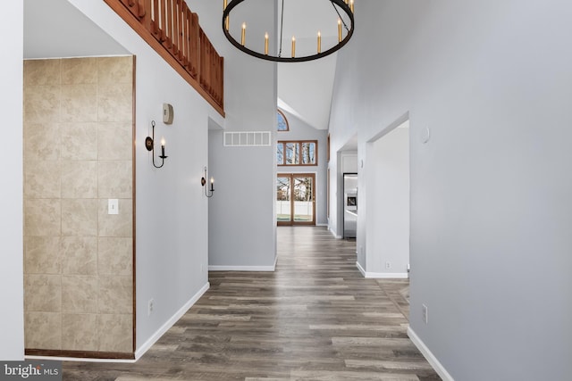 hall with tile walls, a high ceiling, wood-type flooring, and a notable chandelier