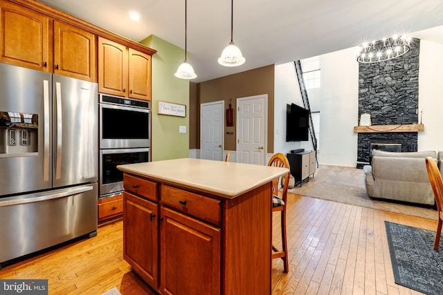 kitchen featuring light wood-type flooring, stainless steel appliances, pendant lighting, a center island, and a stone fireplace