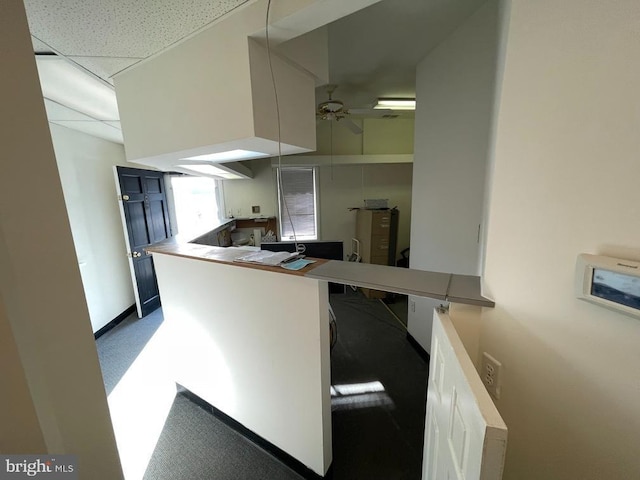 kitchen with kitchen peninsula, a paneled ceiling, ceiling fan, white cabinets, and carpet floors