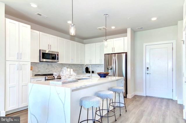 kitchen featuring white cabinetry, sink, stainless steel appliances, pendant lighting, and a kitchen island with sink