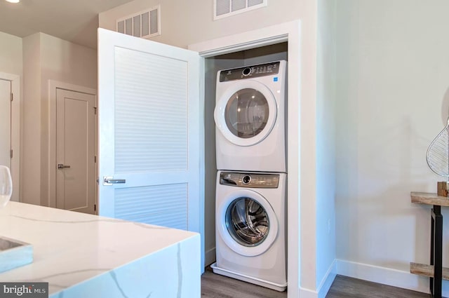 laundry room featuring dark hardwood / wood-style flooring and stacked washing maching and dryer