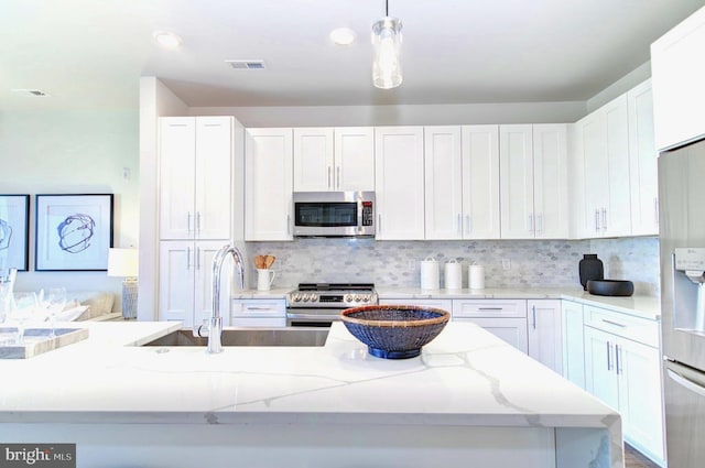 kitchen featuring tasteful backsplash, hanging light fixtures, white cabinets, and stainless steel appliances