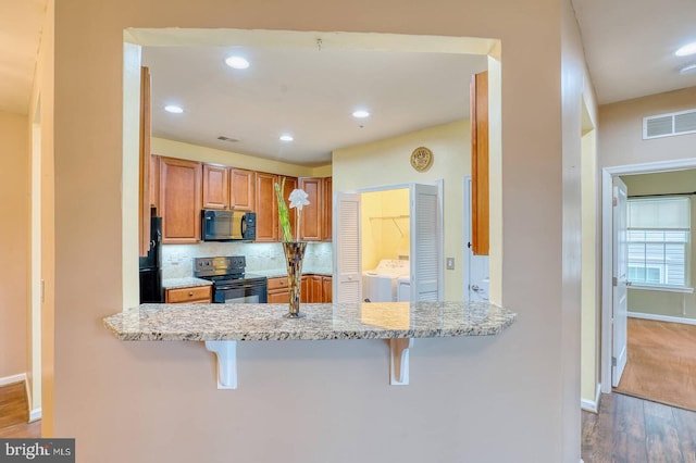 kitchen featuring black appliances, decorative backsplash, washer and dryer, and a breakfast bar area