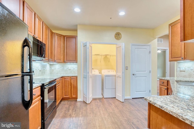 kitchen featuring black appliances, light stone countertops, independent washer and dryer, tasteful backsplash, and light hardwood / wood-style floors