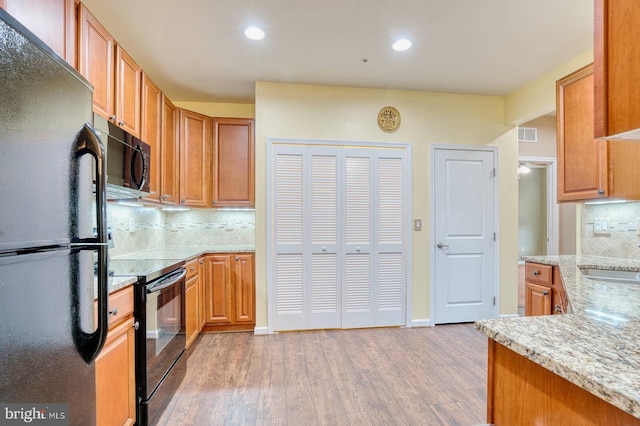 kitchen with light stone countertops, sink, backsplash, light hardwood / wood-style floors, and black appliances