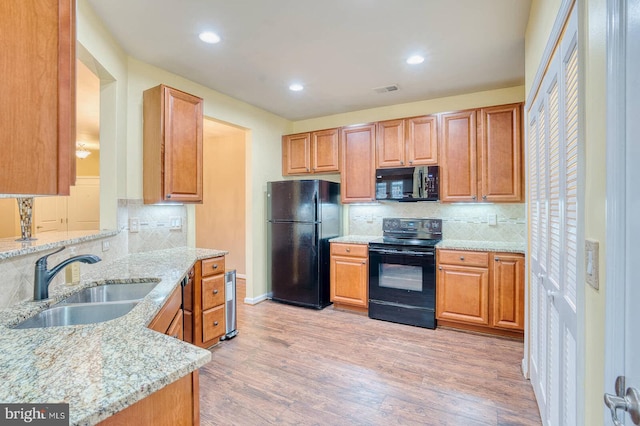 kitchen with black appliances, sink, decorative backsplash, light hardwood / wood-style floors, and light stone counters