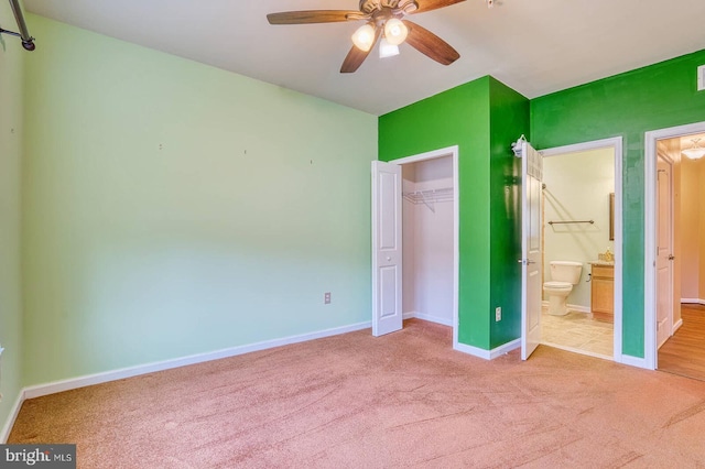 unfurnished bedroom featuring light colored carpet, ensuite bath, a closet, and ceiling fan