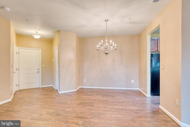 spare room with light hardwood / wood-style floors and a notable chandelier