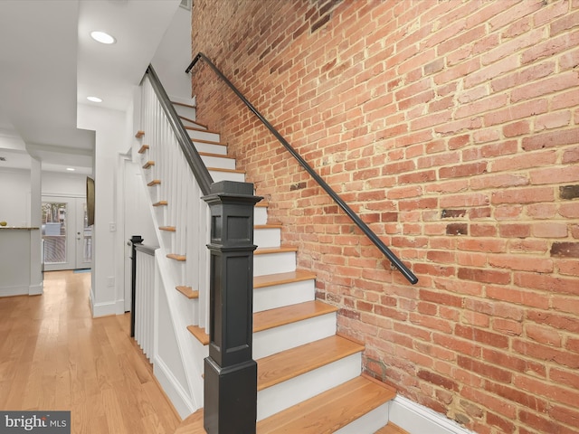 stairs with hardwood / wood-style floors and brick wall