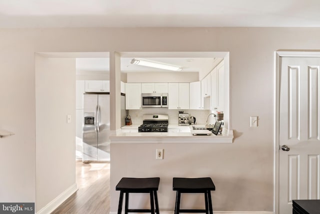 kitchen with light hardwood / wood-style floors, stainless steel appliances, a breakfast bar, white cabinetry, and backsplash