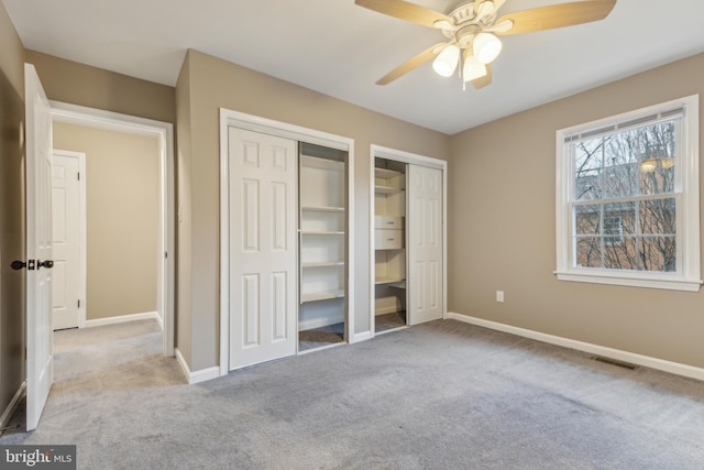 unfurnished bedroom featuring multiple closets, ceiling fan, and light carpet