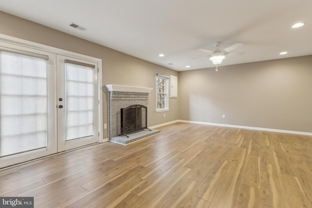 unfurnished living room featuring a brick fireplace, ceiling fan, french doors, and light hardwood / wood-style floors