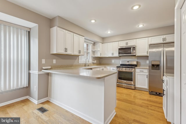 kitchen with kitchen peninsula, white cabinets, appliances with stainless steel finishes, and sink