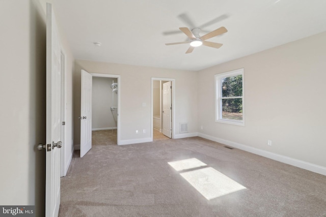 unfurnished bedroom with light carpet, a walk in closet, ensuite bathroom, ceiling fan, and a closet